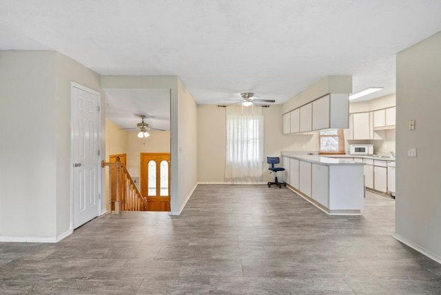 kitchen with ceiling fan, wood finished floors, white microwave, a peninsula, and white cabinetry