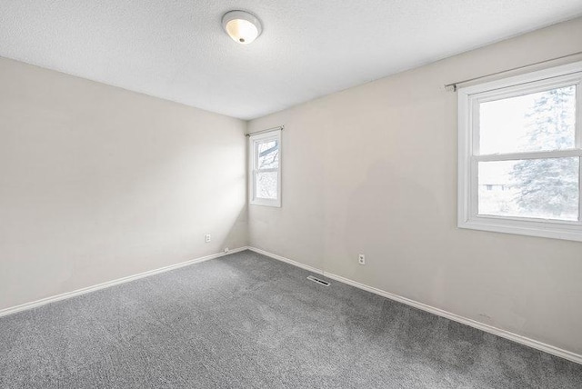 empty room with carpet flooring, a textured ceiling, baseboards, and visible vents