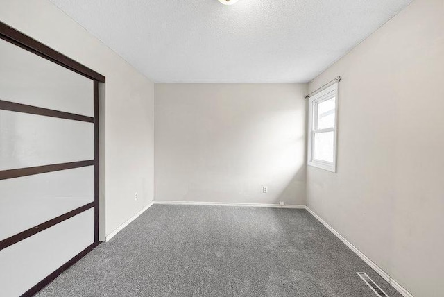 carpeted spare room featuring a textured ceiling, baseboards, and visible vents