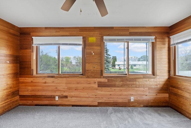 carpeted spare room featuring ceiling fan and wooden walls