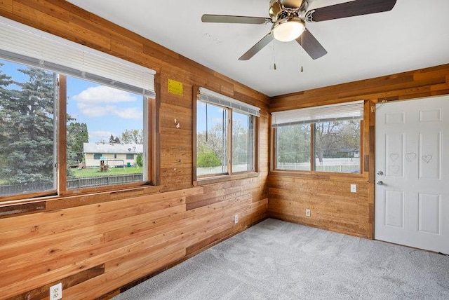 carpeted empty room with a ceiling fan, wooden walls, and a healthy amount of sunlight