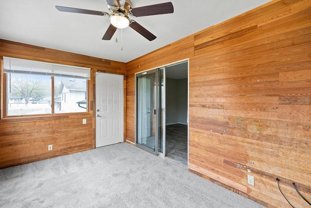 unfurnished room with wooden walls, a ceiling fan, and carpet floors