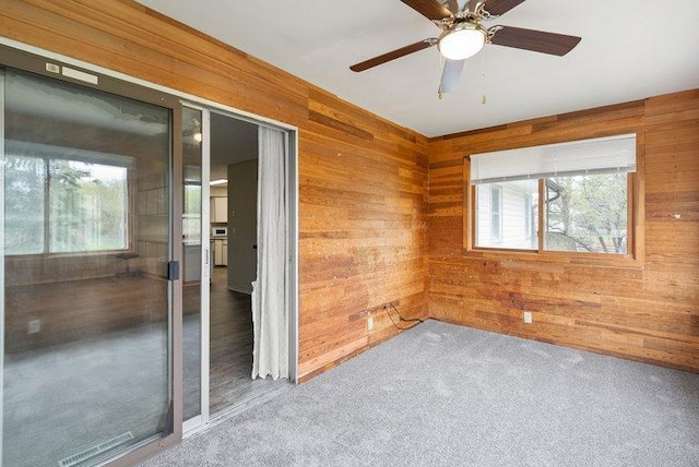 empty room with a ceiling fan, wood walls, and plenty of natural light