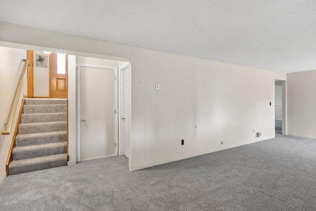 carpeted empty room with stairway, baseboards, and a textured ceiling