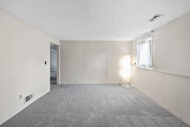 spare room with visible vents, carpet flooring, a textured ceiling, and a decorative wall