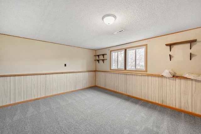 spare room with light colored carpet, a textured ceiling, visible vents, and wooden walls