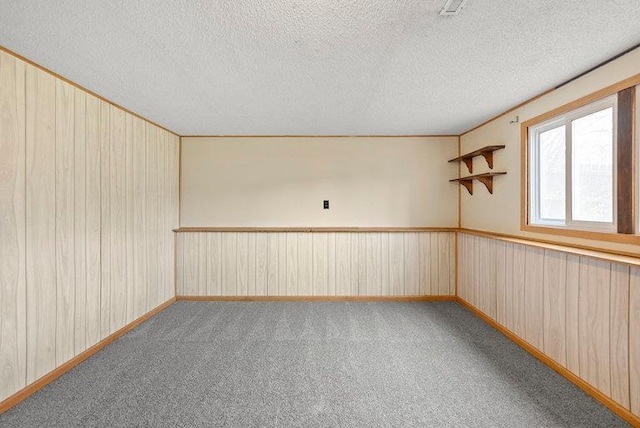 carpeted empty room with a textured ceiling, wood walls, and baseboards