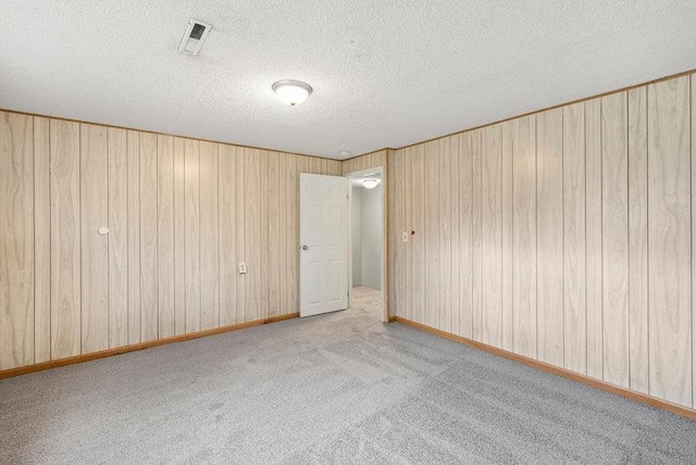 carpeted spare room featuring visible vents, wood walls, and a textured ceiling