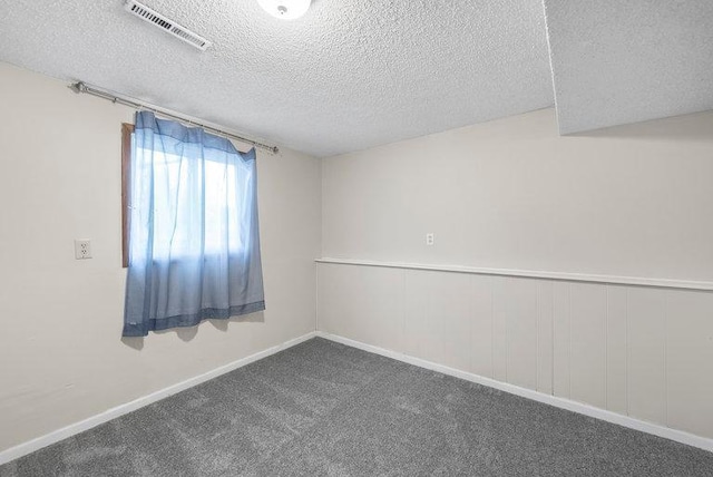 unfurnished room with a textured ceiling, visible vents, baseboards, and dark colored carpet
