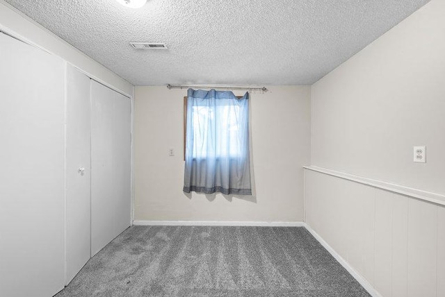carpeted empty room featuring a textured ceiling and visible vents
