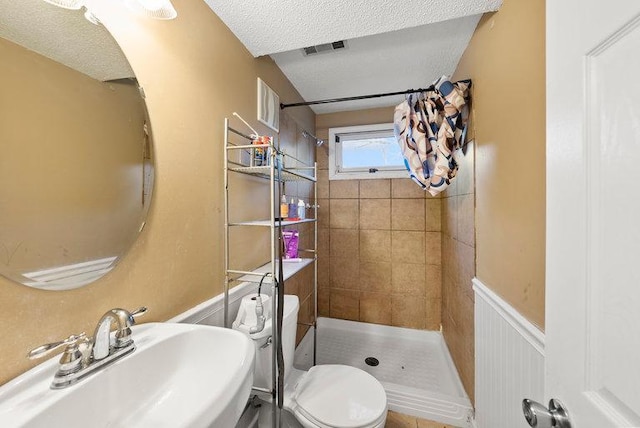 bathroom featuring a sink, a textured ceiling, tiled shower, and visible vents