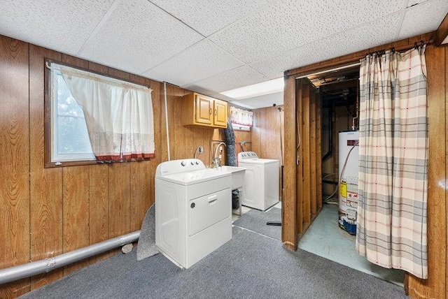 clothes washing area featuring water heater, carpet flooring, wooden walls, and washing machine and clothes dryer