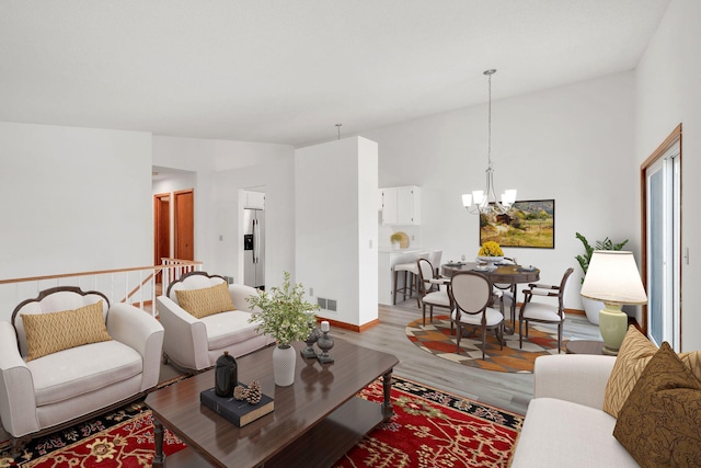 living room featuring light wood-style floors, a chandelier, baseboards, lofted ceiling, and visible vents