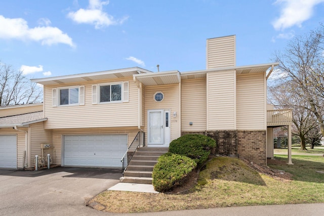 split foyer home with brick siding, a garage, a chimney, and aphalt driveway