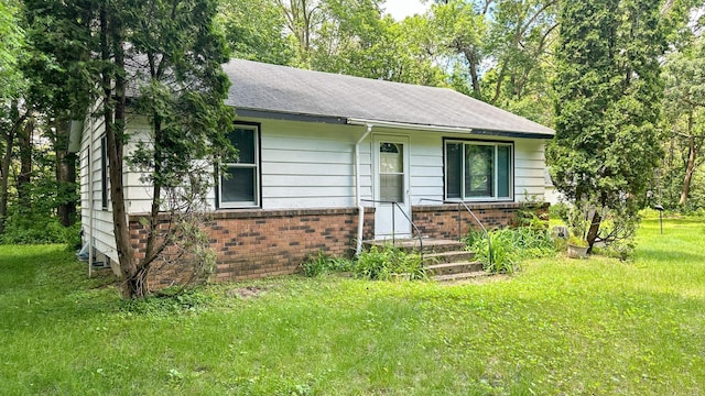 view of front of house with roof with shingles, a front yard, and brick siding