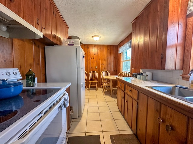 kitchen featuring a sink, under cabinet range hood, wooden walls, white appliances, and a textured ceiling