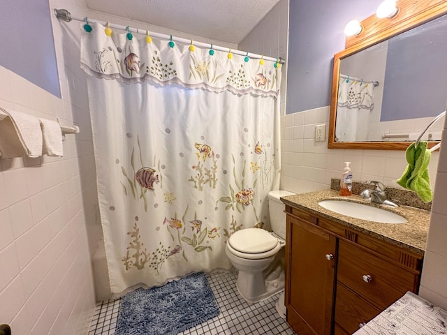 bathroom featuring tile walls, vanity, tile patterned floors, toilet, and a wainscoted wall