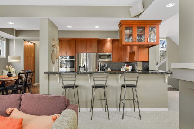 1760 Waterford Ct, Golden Valley, MN 55422 - kitchen featuring glass insert cabinets, decorative backsplash, stainless steel appliances, dark countertops, and a kitchen bar