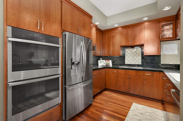 1760 Waterford Ct, Golden Valley, MN 55422 - kitchen with light wood-style flooring, decorative backsplash, brown cabinetry, appliances with stainless steel finishes, and dark countertops