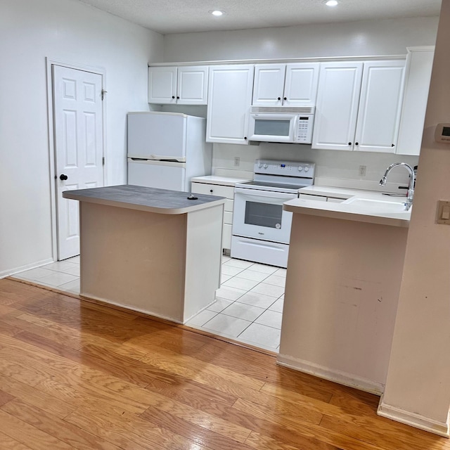 kitchen with a sink, white cabinets, light wood-style floors, and white appliances