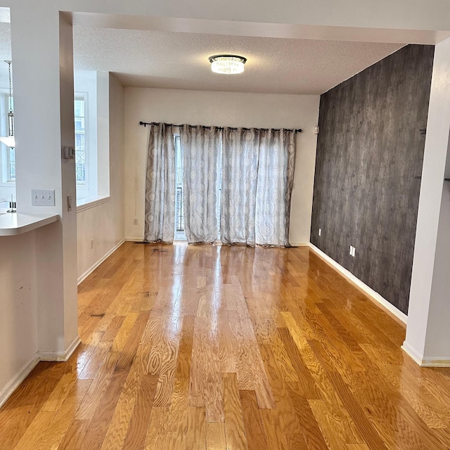 unfurnished room with a textured ceiling, light wood-style flooring, and baseboards