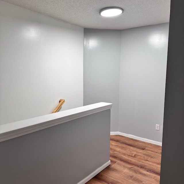 hall featuring an upstairs landing, a textured ceiling, wood finished floors, and baseboards