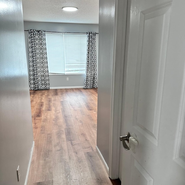 hall featuring baseboards, wood finished floors, and a textured ceiling