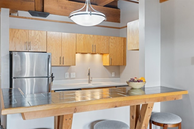kitchen featuring freestanding refrigerator, a sink, a breakfast bar area, and tile countertops