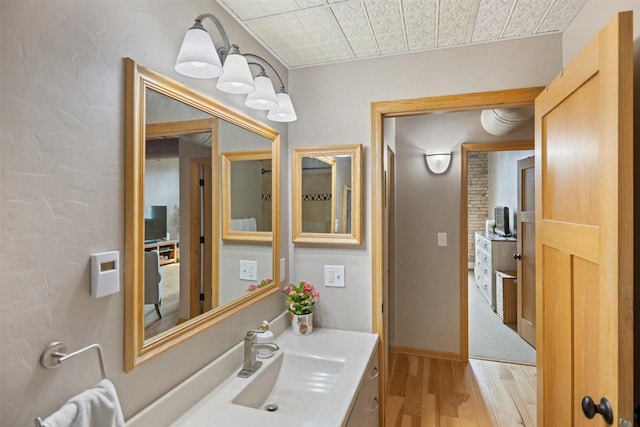 bathroom with wood finished floors, an ornate ceiling, vanity, and baseboards
