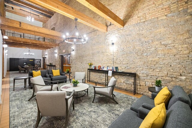 living area with a chandelier, a towering ceiling, beamed ceiling, and wood finished floors