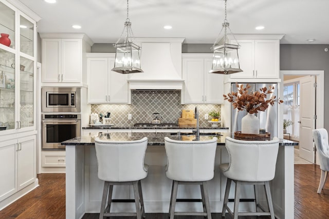 kitchen featuring decorative backsplash, a breakfast bar, stainless steel appliances, dark wood-style flooring, and an island with sink
