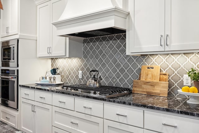 kitchen with appliances with stainless steel finishes, dark stone counters, premium range hood, and white cabinets