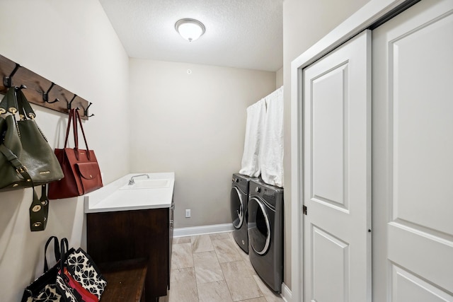 washroom with cabinet space, a sink, independent washer and dryer, baseboards, and a textured ceiling