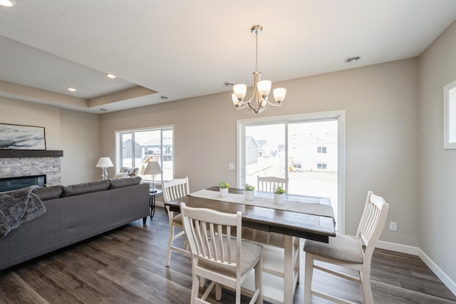 dining area with an inviting chandelier, dark wood-type flooring, visible vents, a stone fireplace, and baseboards