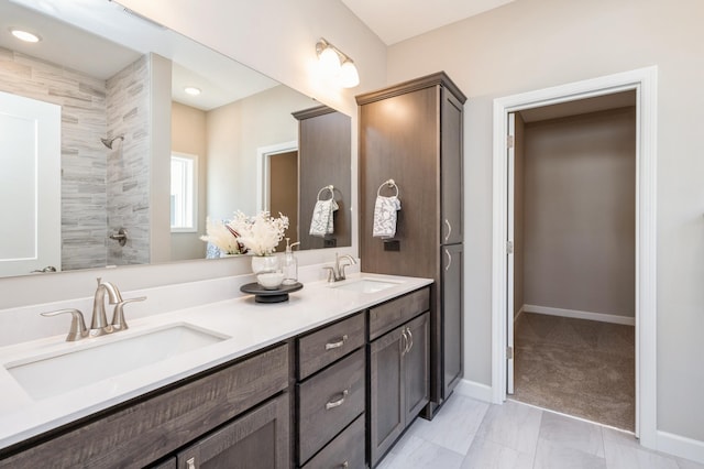 bathroom featuring baseboards, a tile shower, double vanity, and a sink