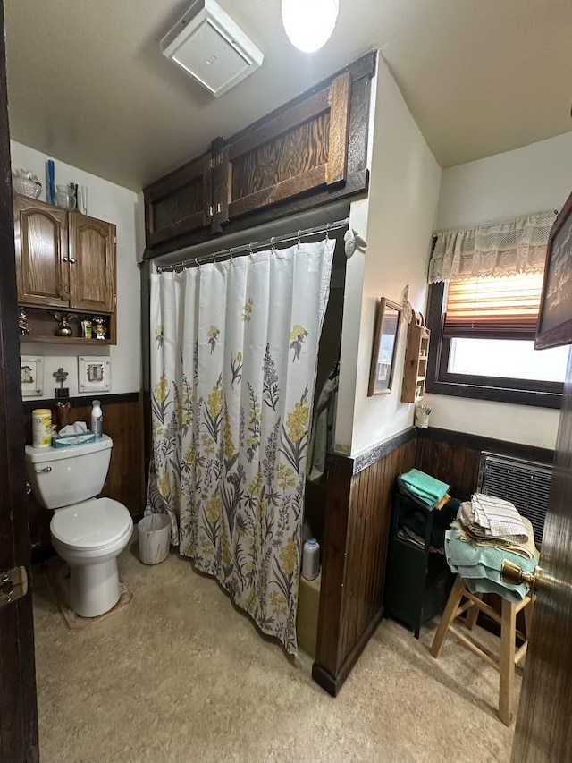 full bath featuring toilet, a shower with curtain, a wainscoted wall, and wooden walls