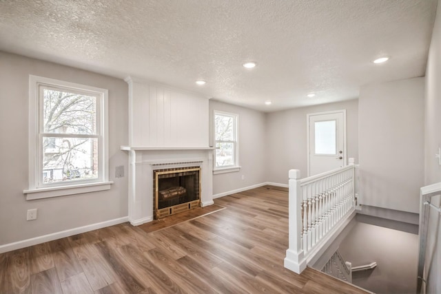 unfurnished living room featuring a tiled fireplace, baseboards, a textured ceiling, and wood finished floors