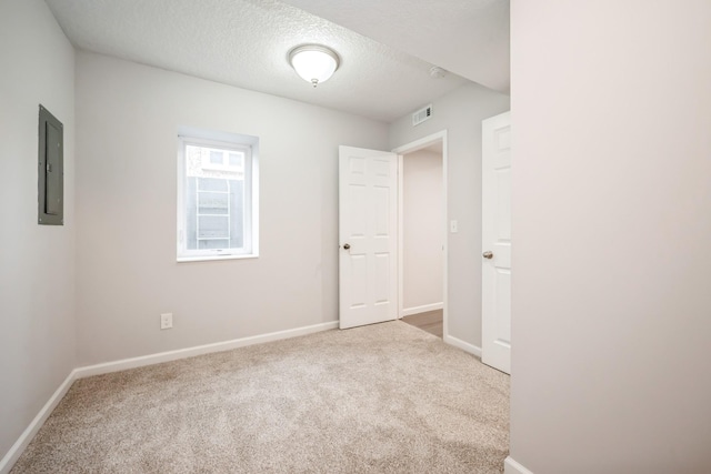 empty room featuring electric panel, a textured ceiling, visible vents, baseboards, and carpet
