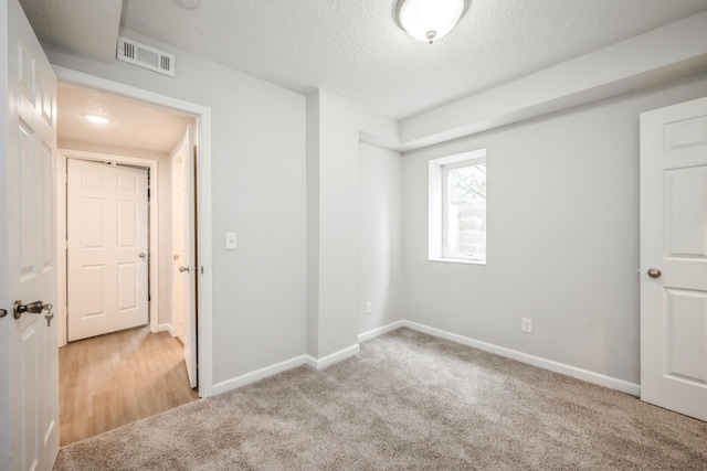 unfurnished room featuring baseboards, light carpet, a textured ceiling, and visible vents
