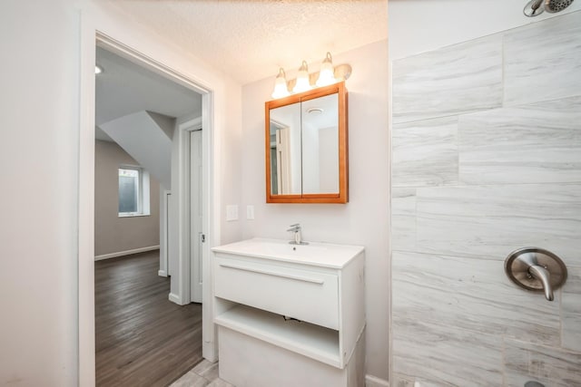 full bathroom featuring a textured ceiling, wood finished floors, vanity, baseboards, and tiled shower
