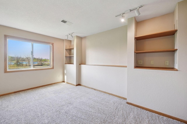 carpeted empty room featuring track lighting, baseboards, and visible vents