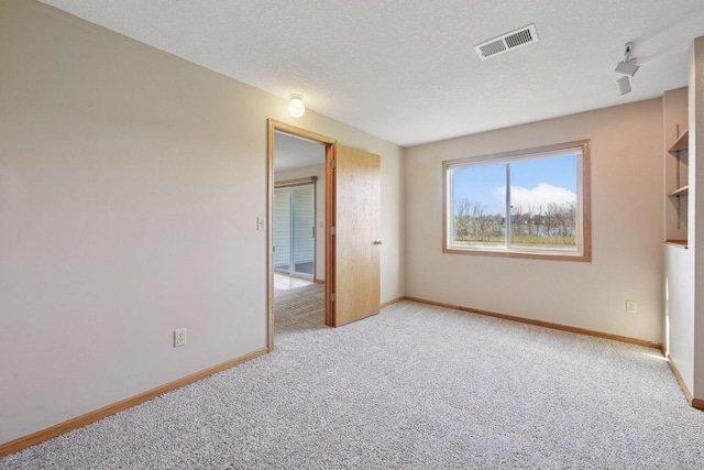carpeted empty room featuring baseboards, a textured ceiling, and visible vents