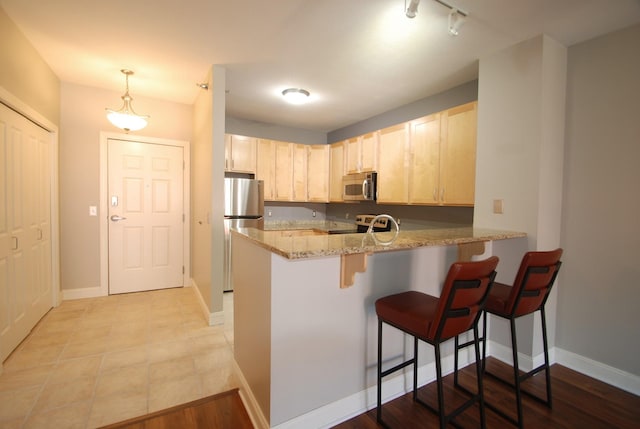 620 Main St N Unit 215, Stillwater, MN 55082 - kitchen with a kitchen bar, light stone countertops, a peninsula, light brown cabinets, and stainless steel appliances