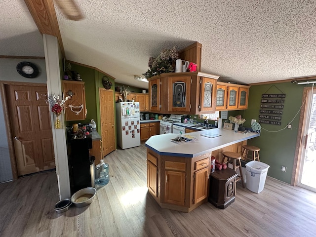 kitchen with a textured ceiling, light wood-style flooring, a peninsula, white appliances, and brown cabinetry