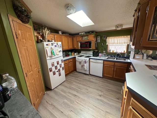 kitchen featuring a sink, light wood-style floors, brown cabinetry, white appliances, and a textured ceiling