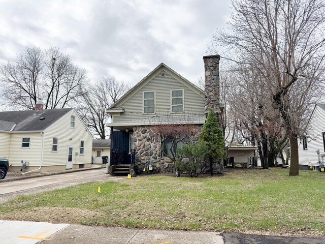 view of front facade featuring a front yard, a chimney, stone siding, and driveway