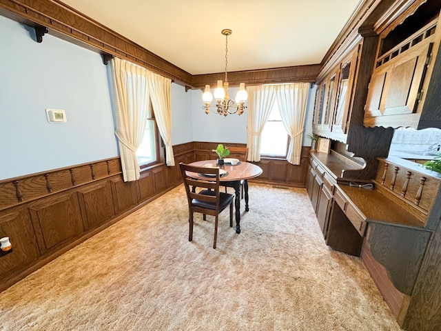 dining area featuring a chandelier, a wainscoted wall, and light colored carpet