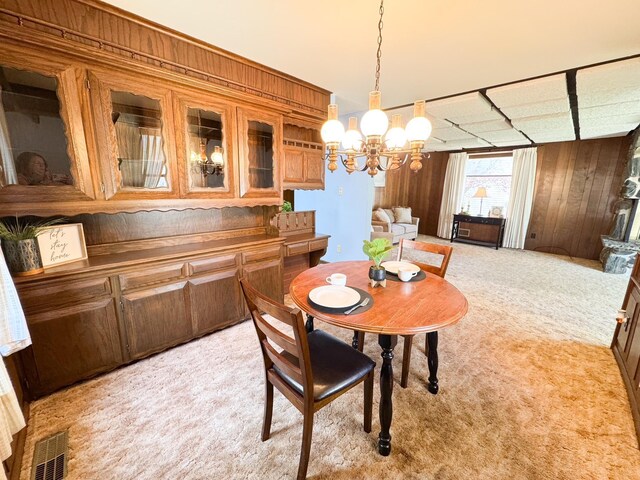 dining room with light carpet, wooden walls, and a chandelier