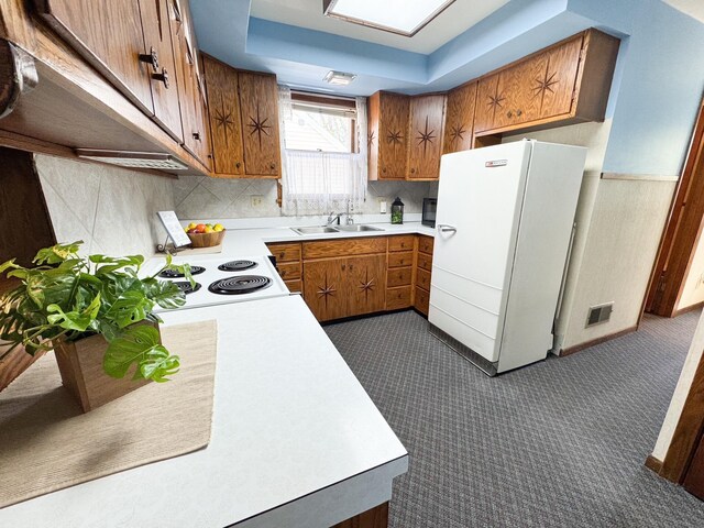 kitchen with freestanding refrigerator, brown cabinets, a sink, light countertops, and a tray ceiling