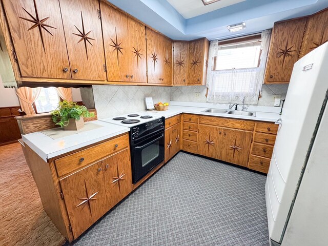 kitchen with black range with electric cooktop, a sink, freestanding refrigerator, brown cabinetry, and light countertops